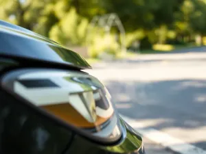 Dłoń w rękawicy zakłada czystą, metalową klemę na biegun akumulatora samochodowego w warsztatowym otoczeniu.